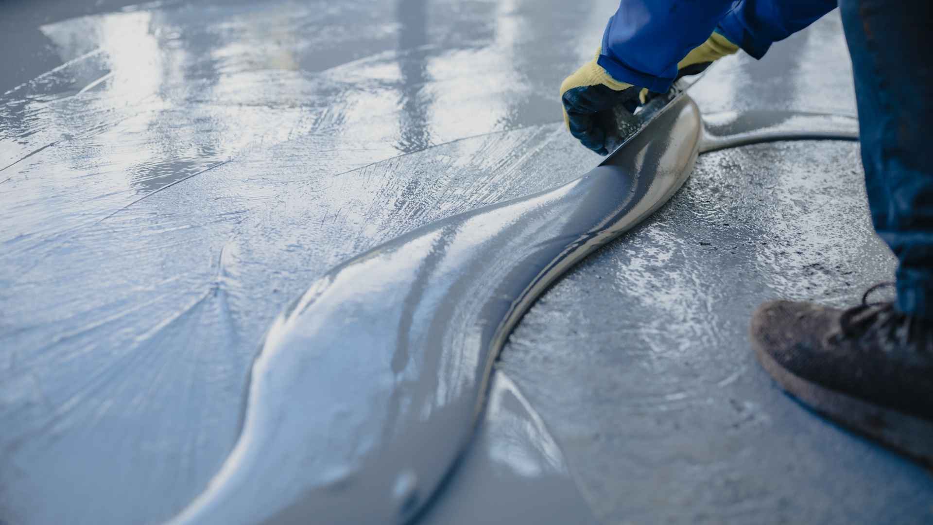 Person smoothing wet concrete floor with tool