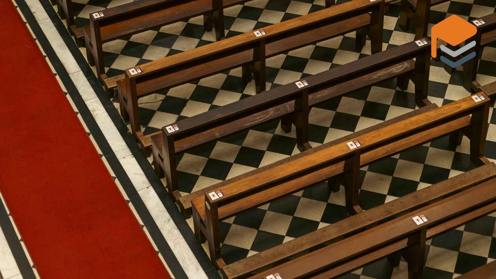 Wooden pews on checkered floor with red carpet inside a church
